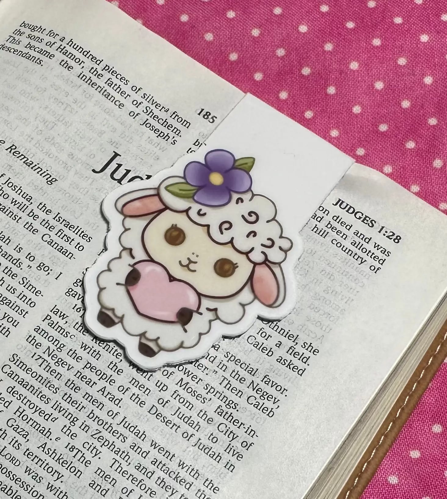 Illustrated sheep with a flower on a page of text, with a pink polka dot fabric background.