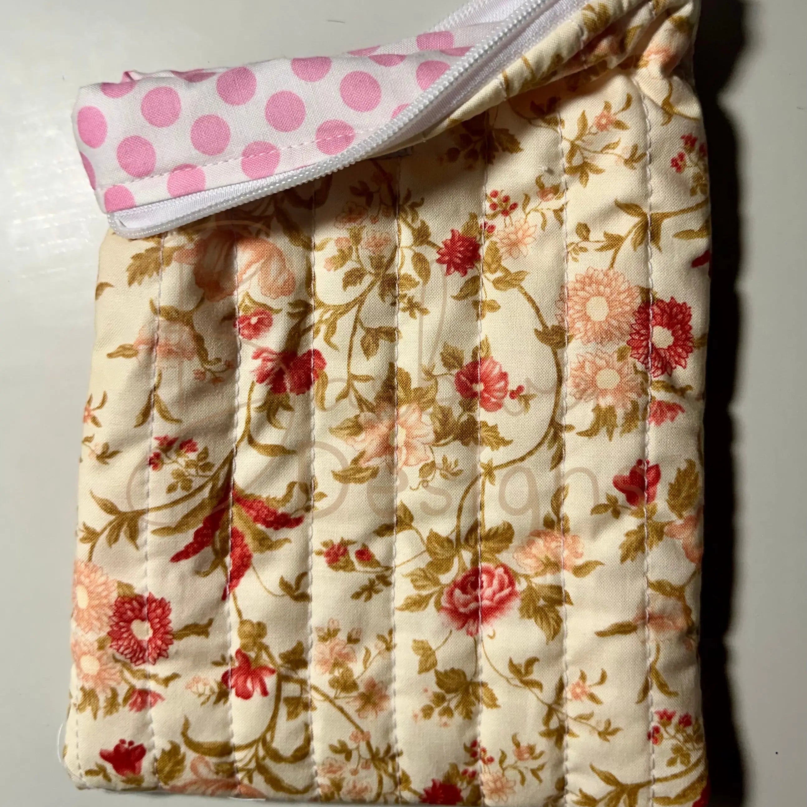 Floral-patterned quilted item with a pink polka dot cover on a light background