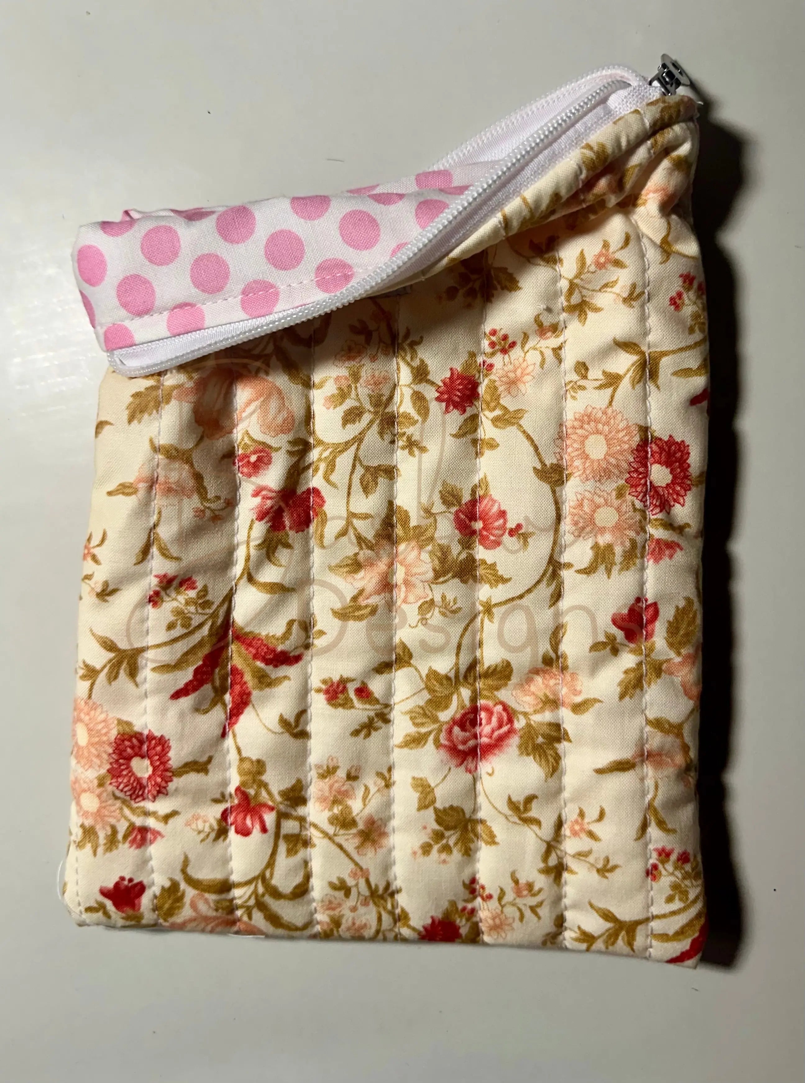 Floral-patterned quilted item with a pink polka dot cover on a light background